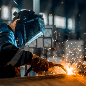 An industrial technician fuses metalwork pipe while wearing a face guard.