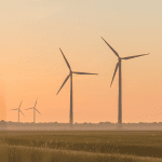 Wind energy turbines stand against an orange sunset sky.