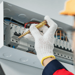 A screwdriver is used to adjust something in an electricity panel mounted on the wall.
